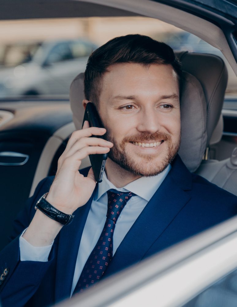 Happy company manager listening to his employee on topic of financial gain, hearing about high amount of profit possibilities, ready to go and make money, riding in back of luxury car